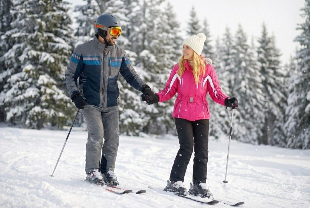 Pareja esquiando de la mano con ropa de nieve de colores brillantes en una pista de esquí.